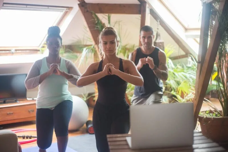 Grupo diverso praticando exercícios em casa guiados por vídeo em um laptop