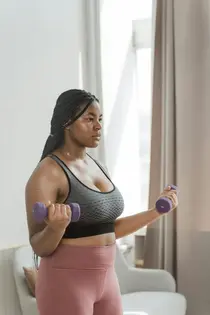 Mulher com tranças suando, fazendo exercícios em casa com halteres roxos