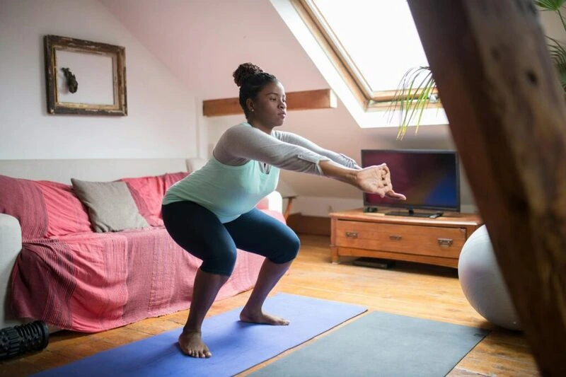 Mulher realizando agachamento em colchonete na sala de estar, praticando exercício em casa