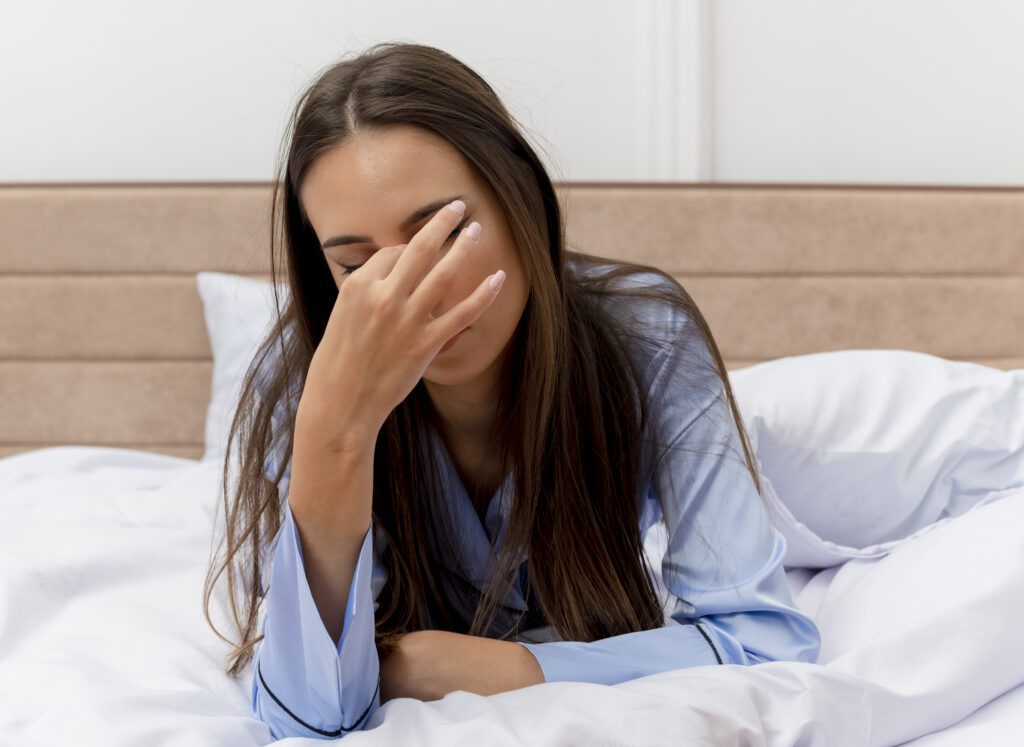 mulher bonita de pijama azul deitada na cama com travesseiro bocejano